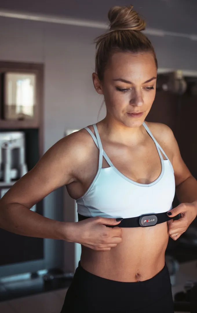 Woman adjusting a black heart rate monitor chest strap before an indoor workout | Polar Philippines