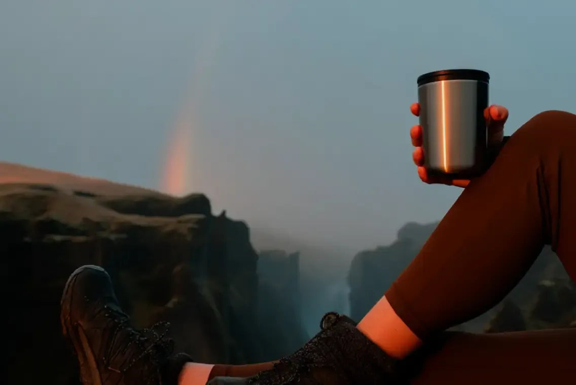 Woman sitting on mountain rocks holding a mug with scenic outdoor view | Polar Philippines