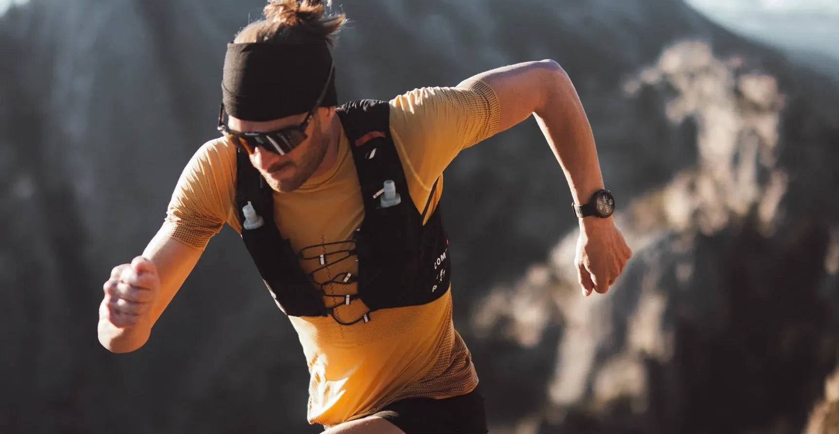Person running on a mountain trail wearing a yellow shirt,advance gps smart watch and black backpack.